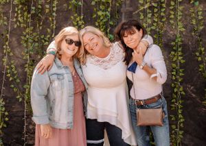 Group of people posing together against a wall with hanging green vines wearing coordinated casual outfits.