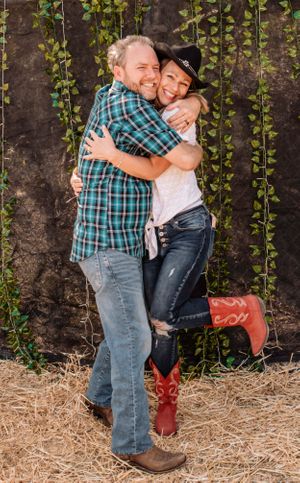 Couple in casual western wear sharing affectionate moment against vine-covered wall.