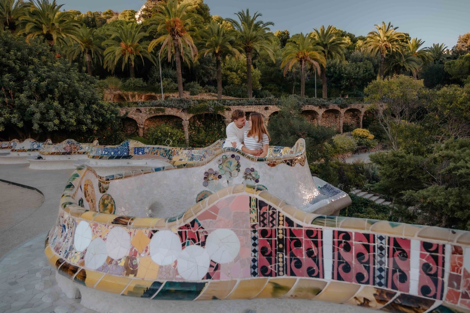 Couple holding hands walking through the stone columns of Park Güell.