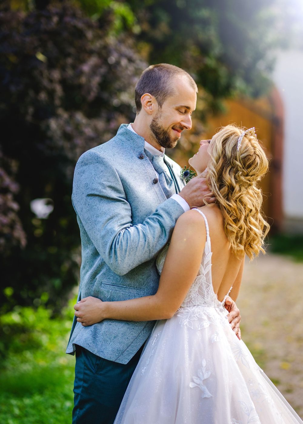 A couple in wedding attire share a romantic moment in a garden setting with natural lighting and greenery.