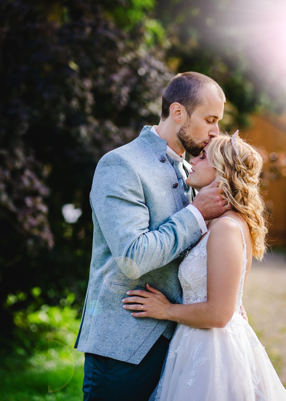 A romantic wedding couple shares tender kisses in a garden setting with soft lighting and natural greenery.
