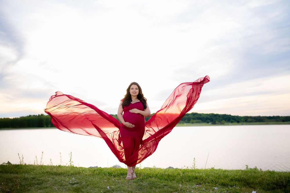 Woman in flowing red dress dances gracefully against scenic lake and sky backdrop at sunset.