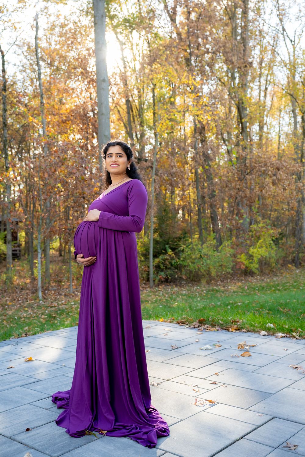 A collection of maternity portraits featuring someone in a flowing purple gown posing on a stone patio surrounded by fall trees.