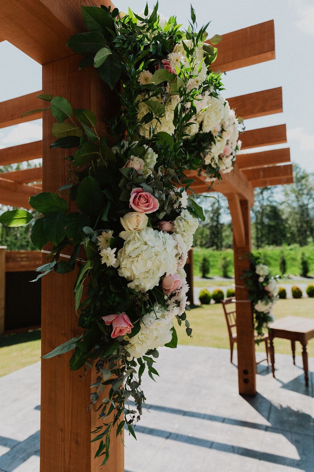 Wooden wedding pergola post decorated with lush white hydrangeas and pink roses in garden setting.