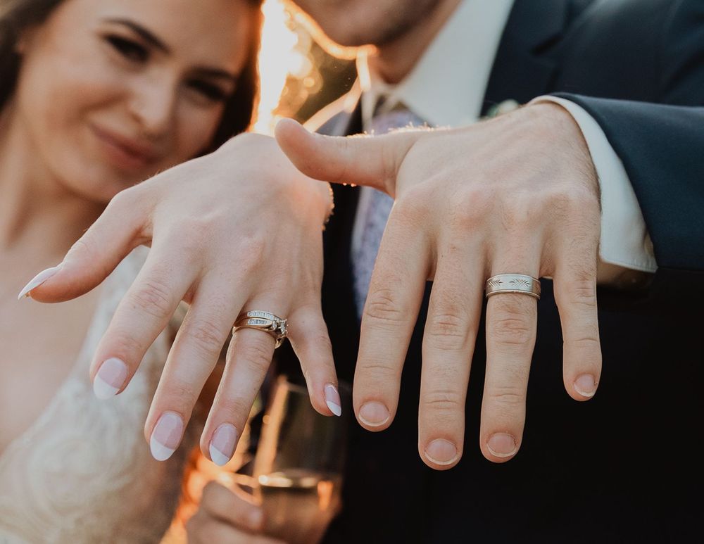 Newlywed couple displaying their matching silver wedding bands on their hands in a close-up romantic photo.
