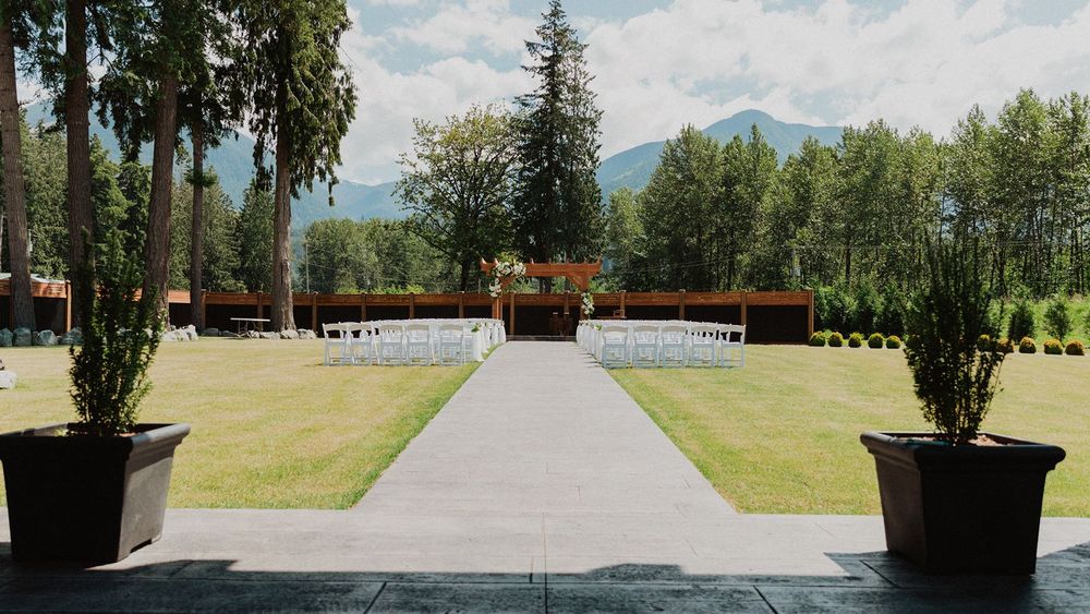 Elegant outdoor wedding ceremony aisle with white chairs and mountain backdrop.