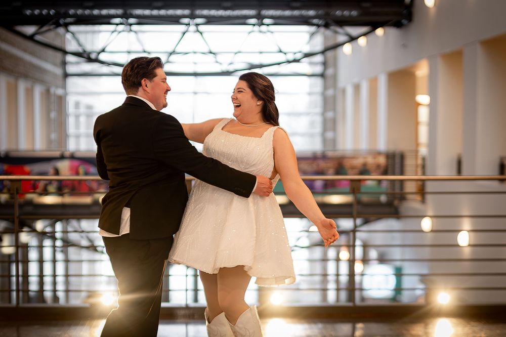 A couple dances together in a warmly lit indoor venue with a modern industrial style hallway setting.