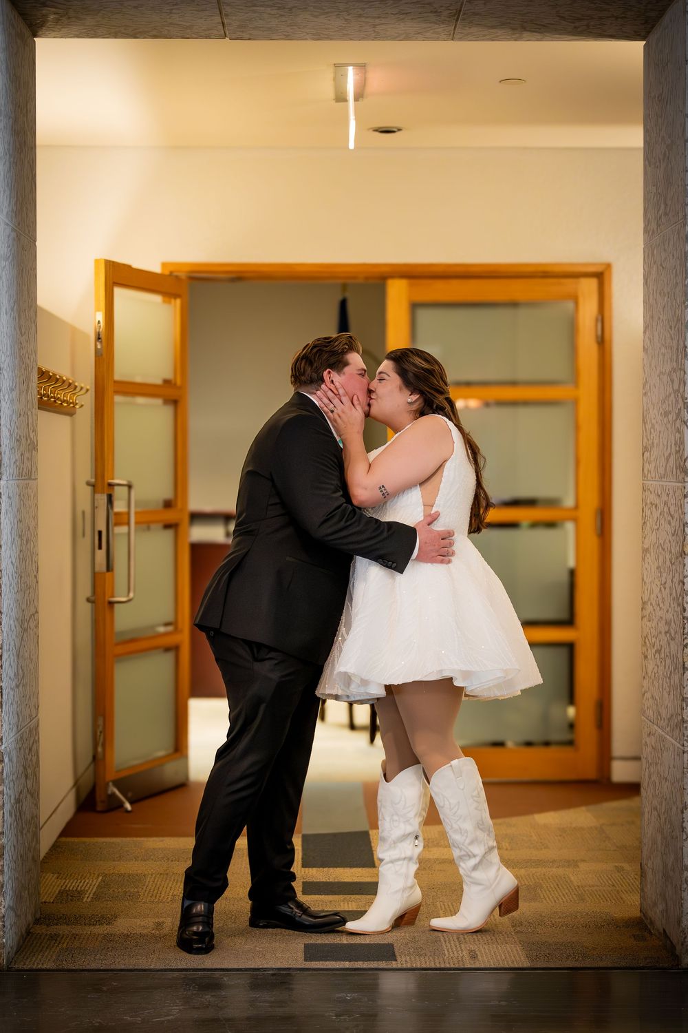 A couple shares a romantic dip kiss in a modern indoor hallway setting.