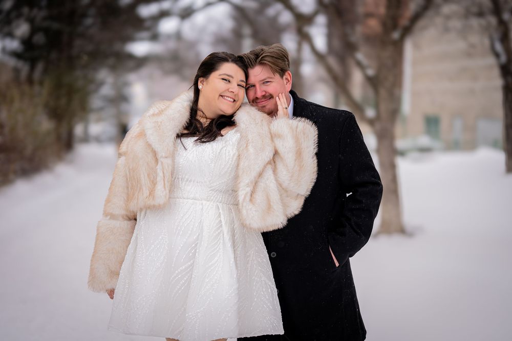 A couple embraces tenderly in a snowy winter landscape during their wedding photoshoot.