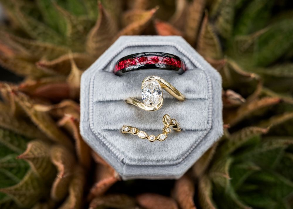 Gold wedding rings with diamonds and ruby band displayed in a gray velvet octagonal ring box.