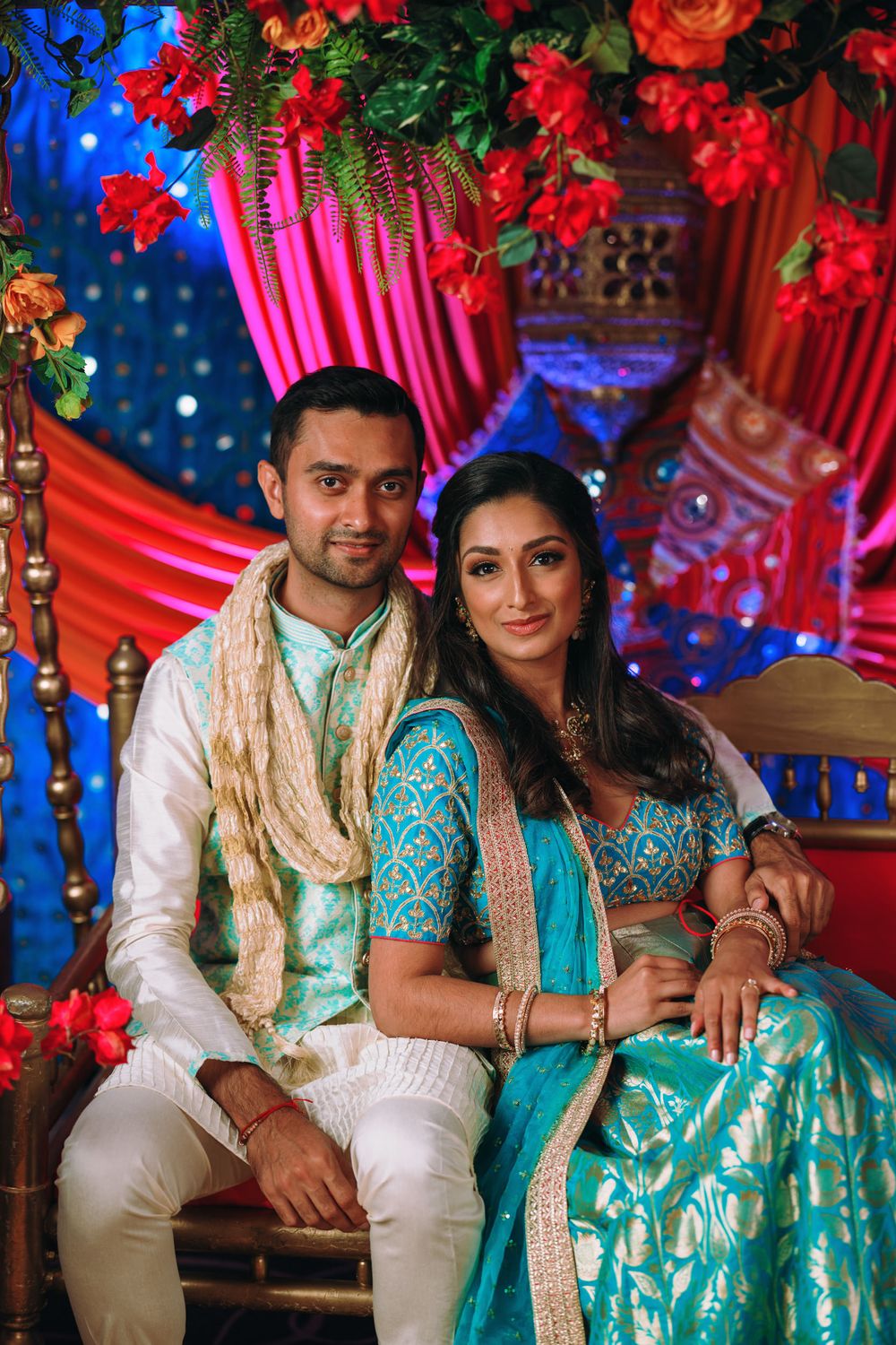 Couple in coordinating turquoise and white traditional Indian outfits pose together at decorated wedding venue.