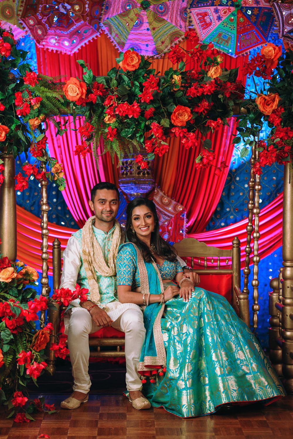 Traditional Indian wedding decor features vibrant red drapes, floral arrangements and turquoise accents against ornate backdrop.