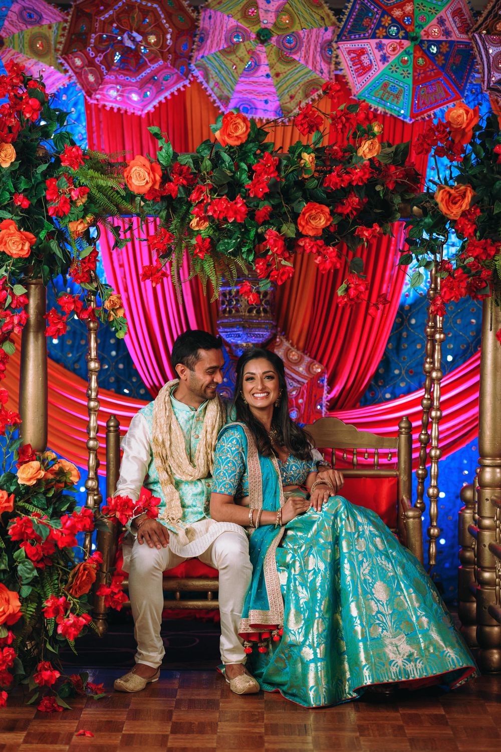 Colorful Indian wedding decor with red drapes, floral arrangements and turquoise accents creates a vibrant celebration atmosphere.
