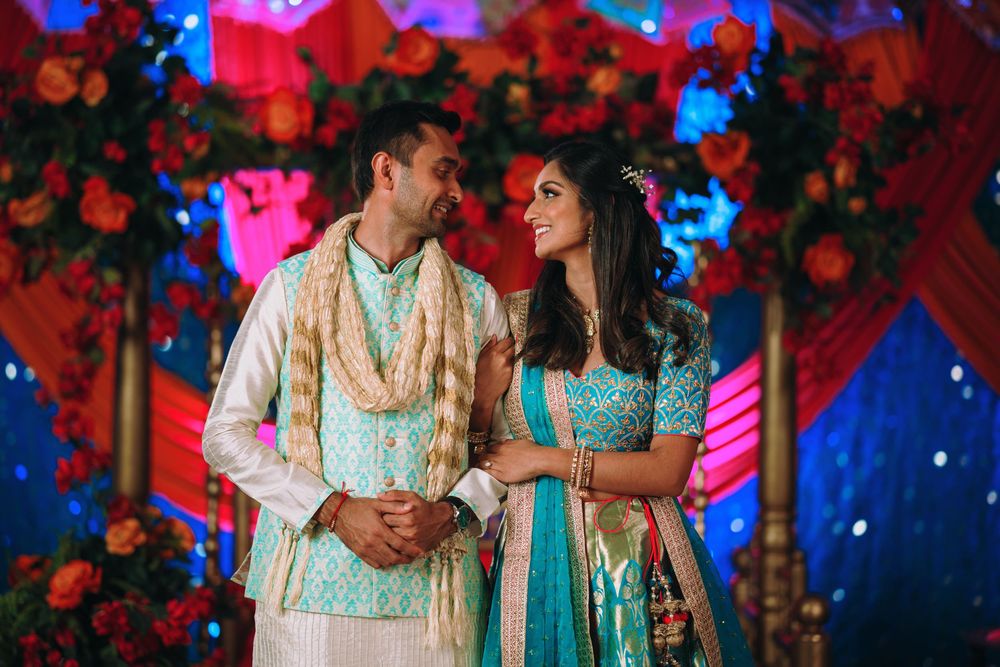 A colorful Indian wedding celebration with vibrant red and blue lighting and floral decorations in the background.
