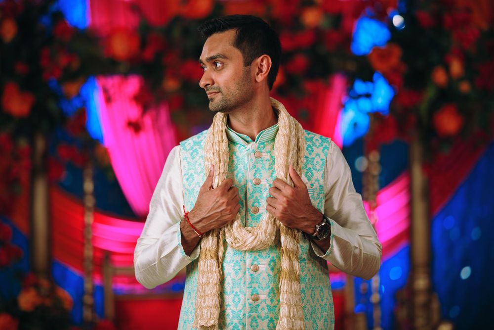 A person in traditional Indian attire performs dance movements against a colorful red and blue backdrop.