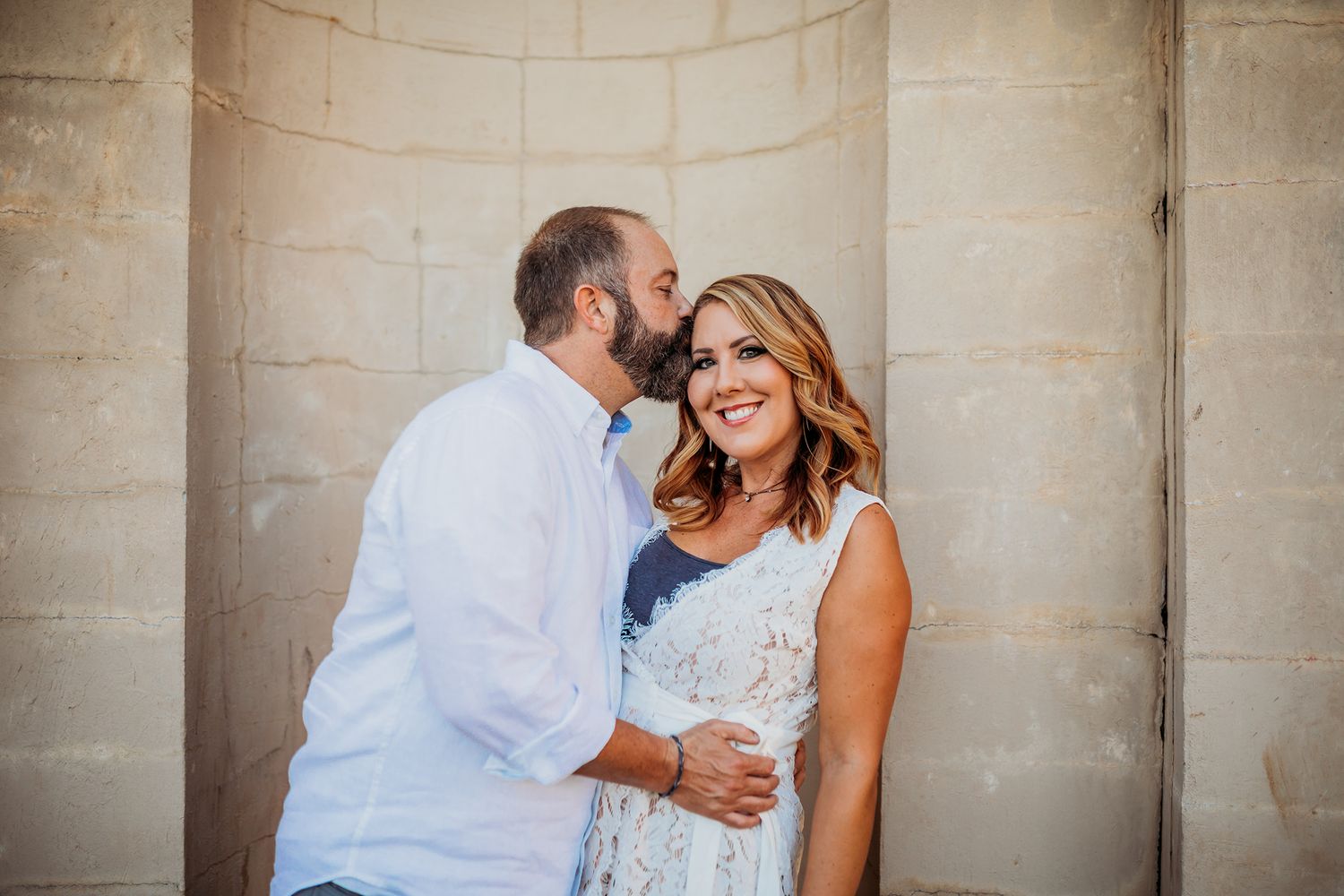Romantic engagement photo session against a light stone wall background.