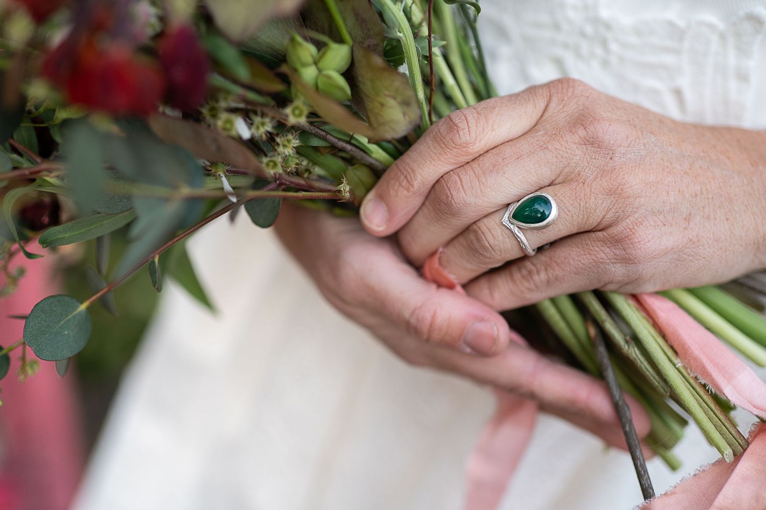 Close up of bride's hand holding bouquet. She wears a green ring by Elizabeth Terzza jewellery