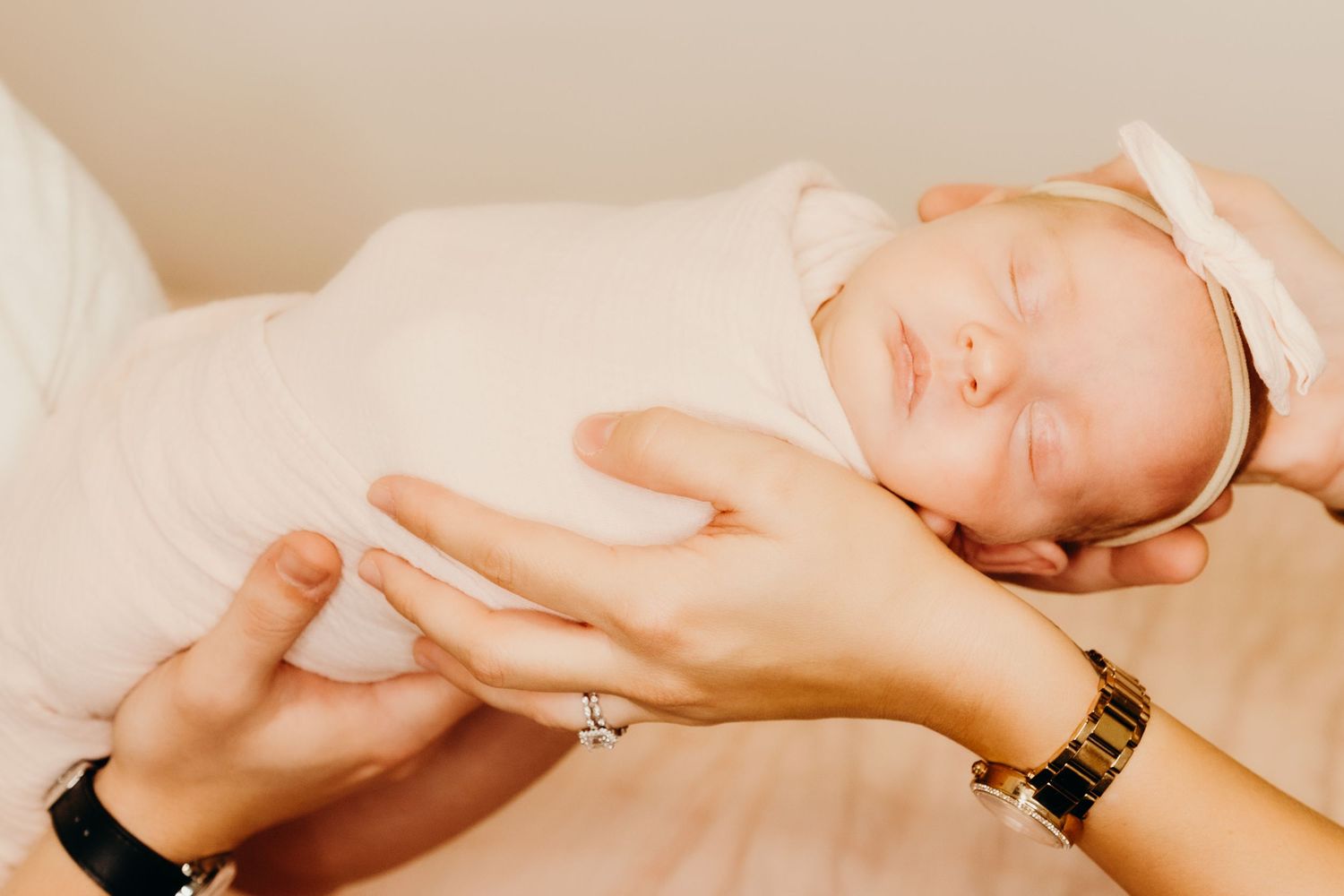 Sleeping newborn in white wrap being cradled by hands with jewelry.