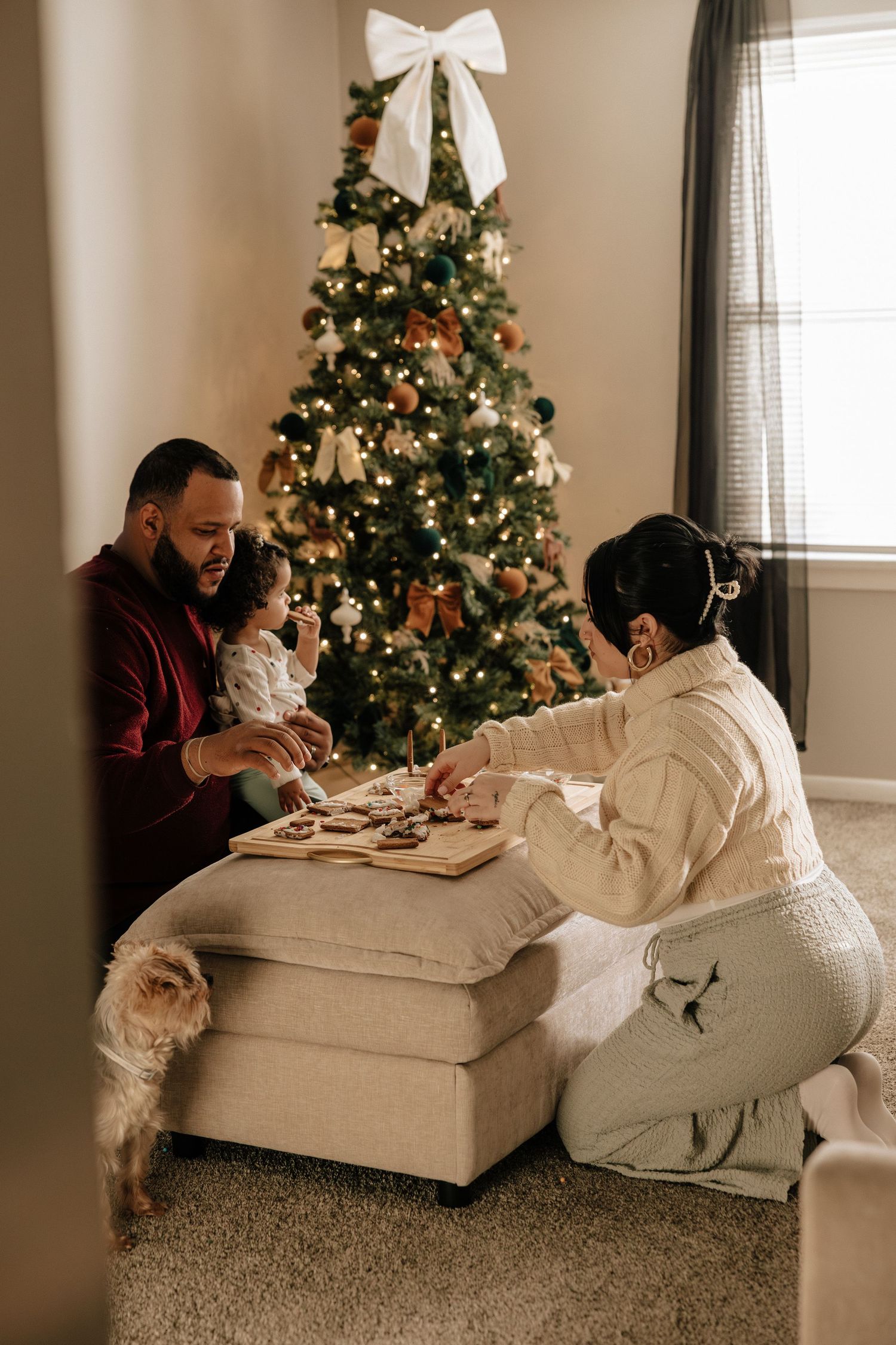 A couple relaxes on a cozy white couch during the holiday season with decorated Christmas trees in the background.