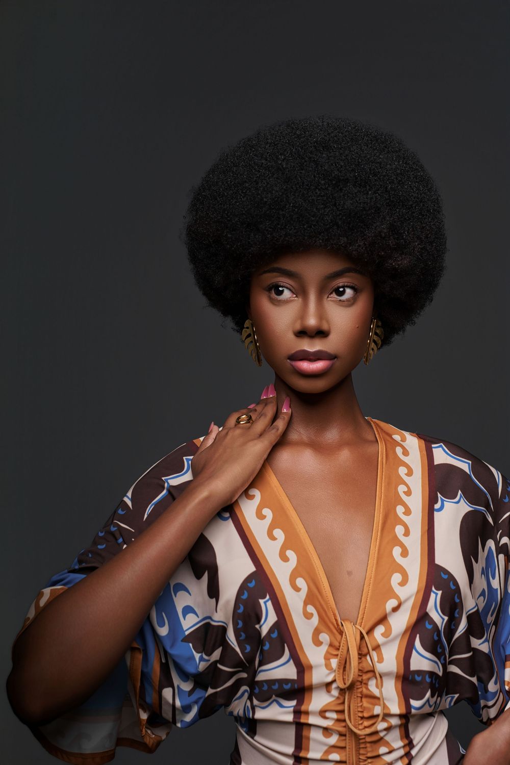 Fashion portrait showing model wearing a patterned dress with white trim and natural curly hair against dark background.