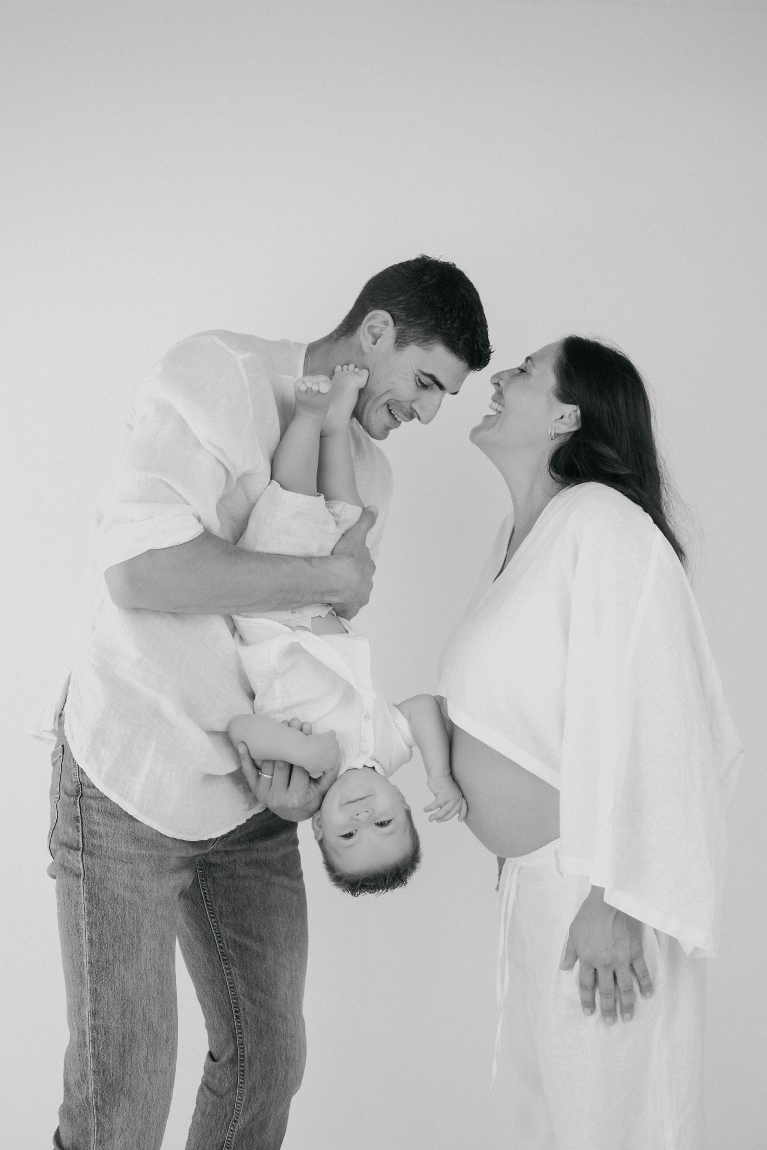 Family shares intimate black and white moment together against neutral background in studio setting.