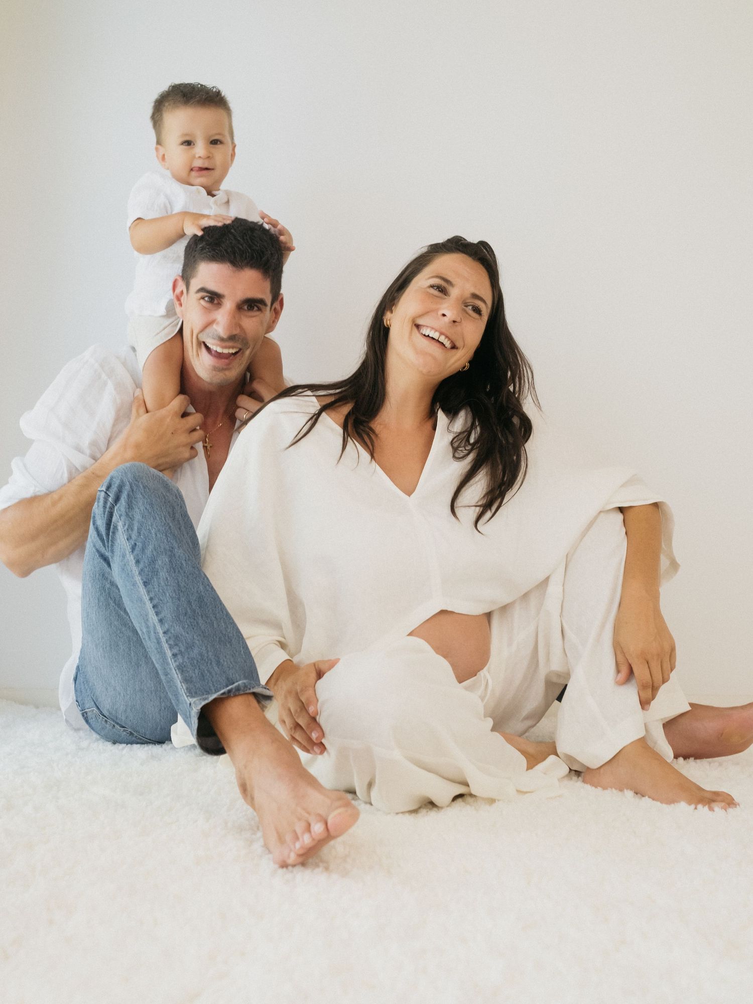 Family relaxing together on white floor wearing casual clothing in minimalist setting.