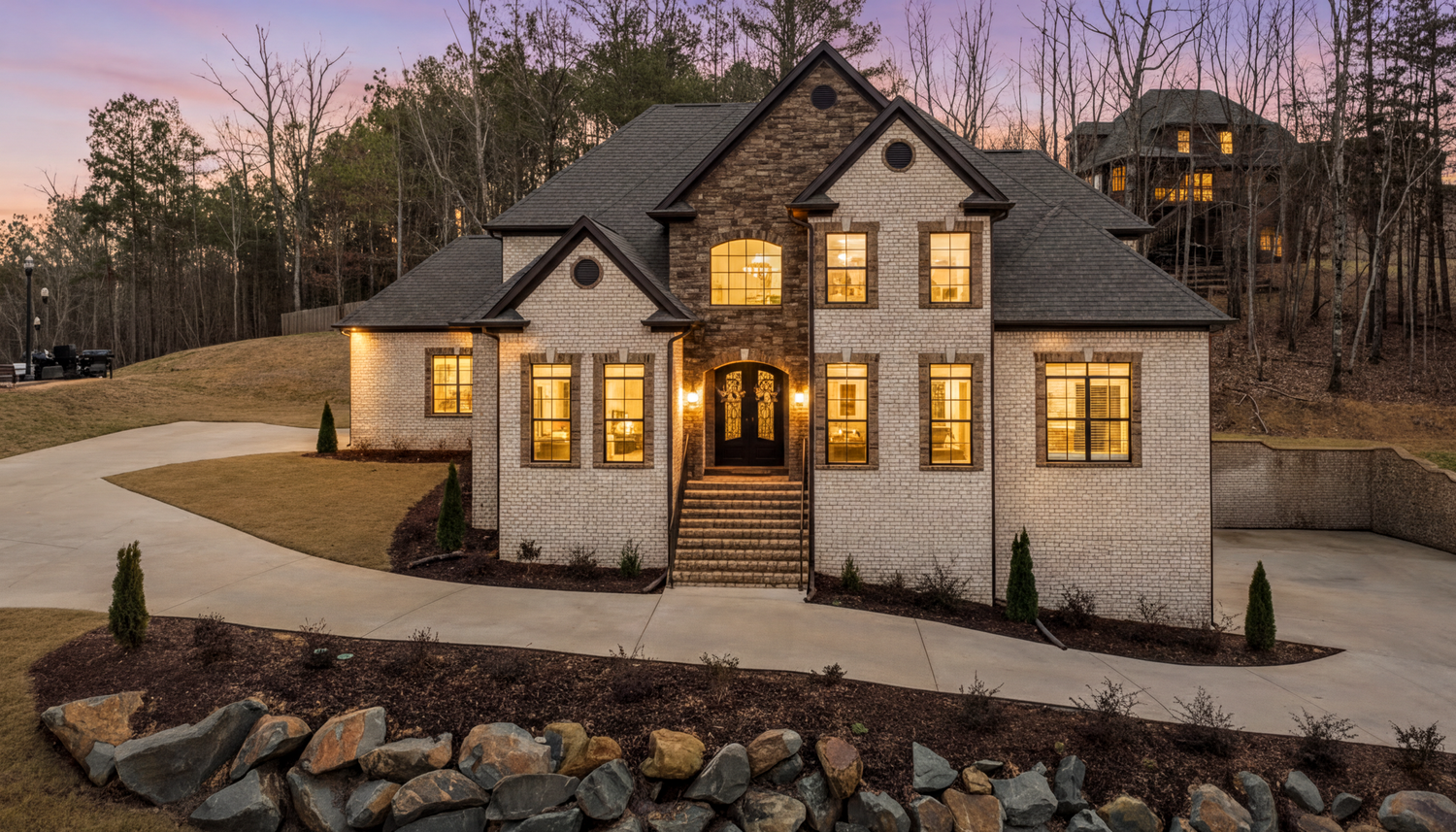 Professional daylight exterior photo of a Birmingham, AL luxury home with stone and brick siding, a curved driveway, and tiered landscaping.
