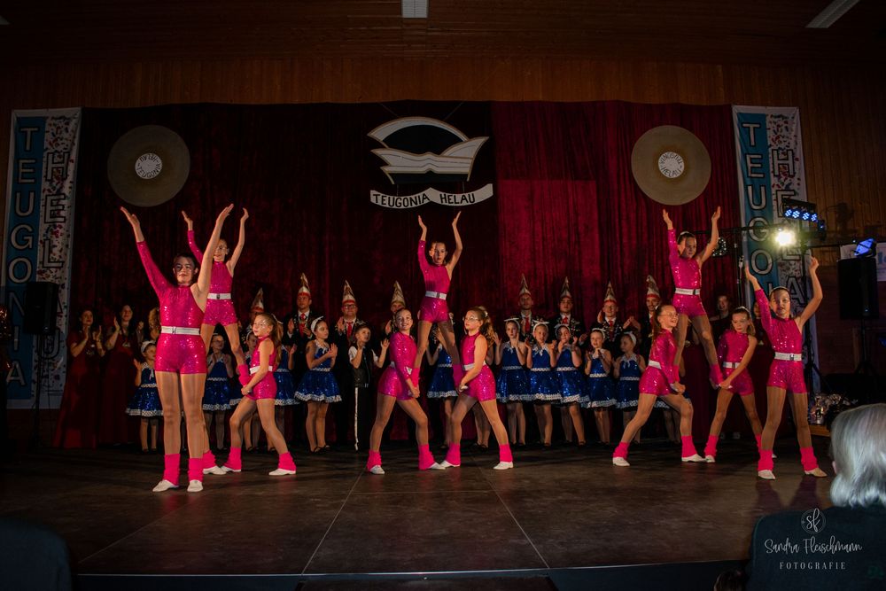 Dance performers in vibrant pink costumes perform synchronized movements on a dark stage.