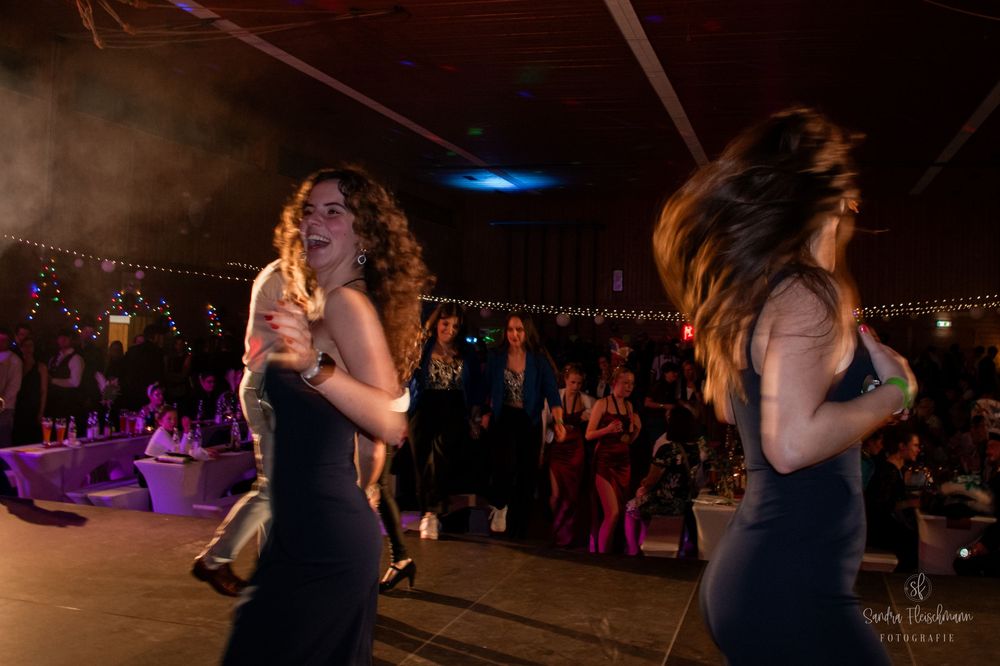 People dancing at a nighttime event with purple lighting and a city skyline visible in the background.