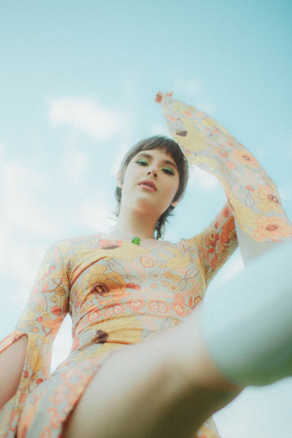 Person in a peach floral dress poses against a bright blue sky background.
