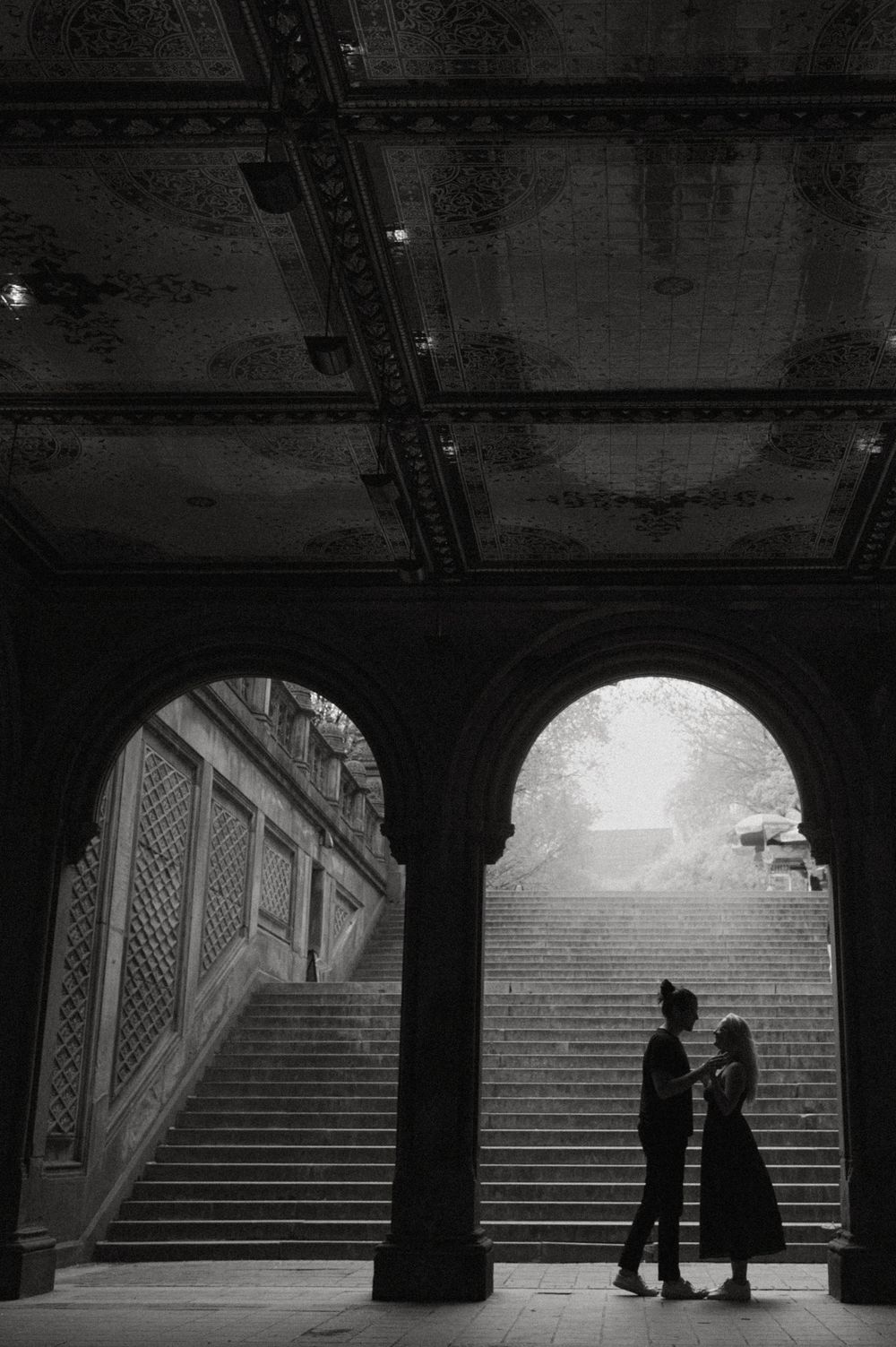 Silhouettes of people under arched passageway with dramatic staircase lighting.