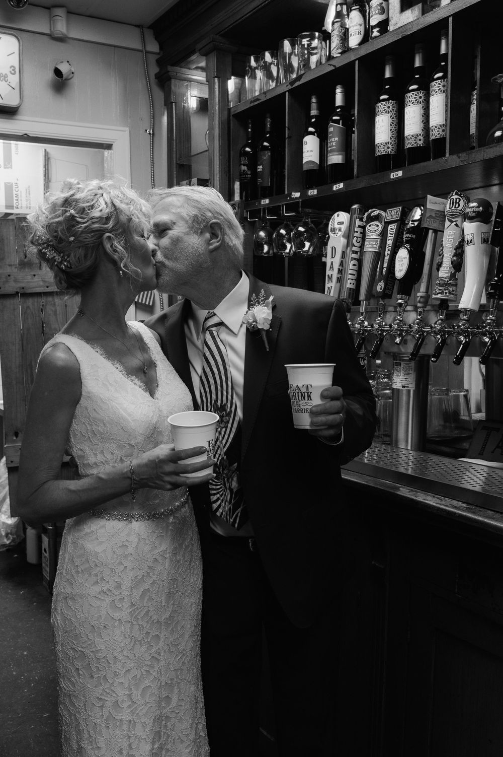 A couple dances together at a bar with bottles and glassware visible in the background.