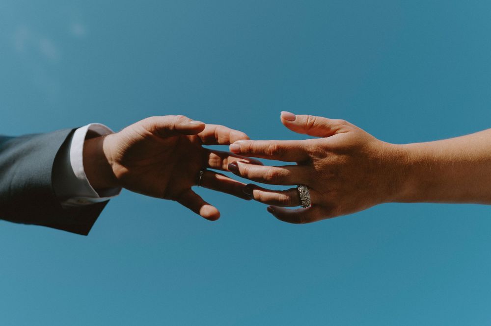 Two hands reaching to exchange something against a bright blue sky background.
