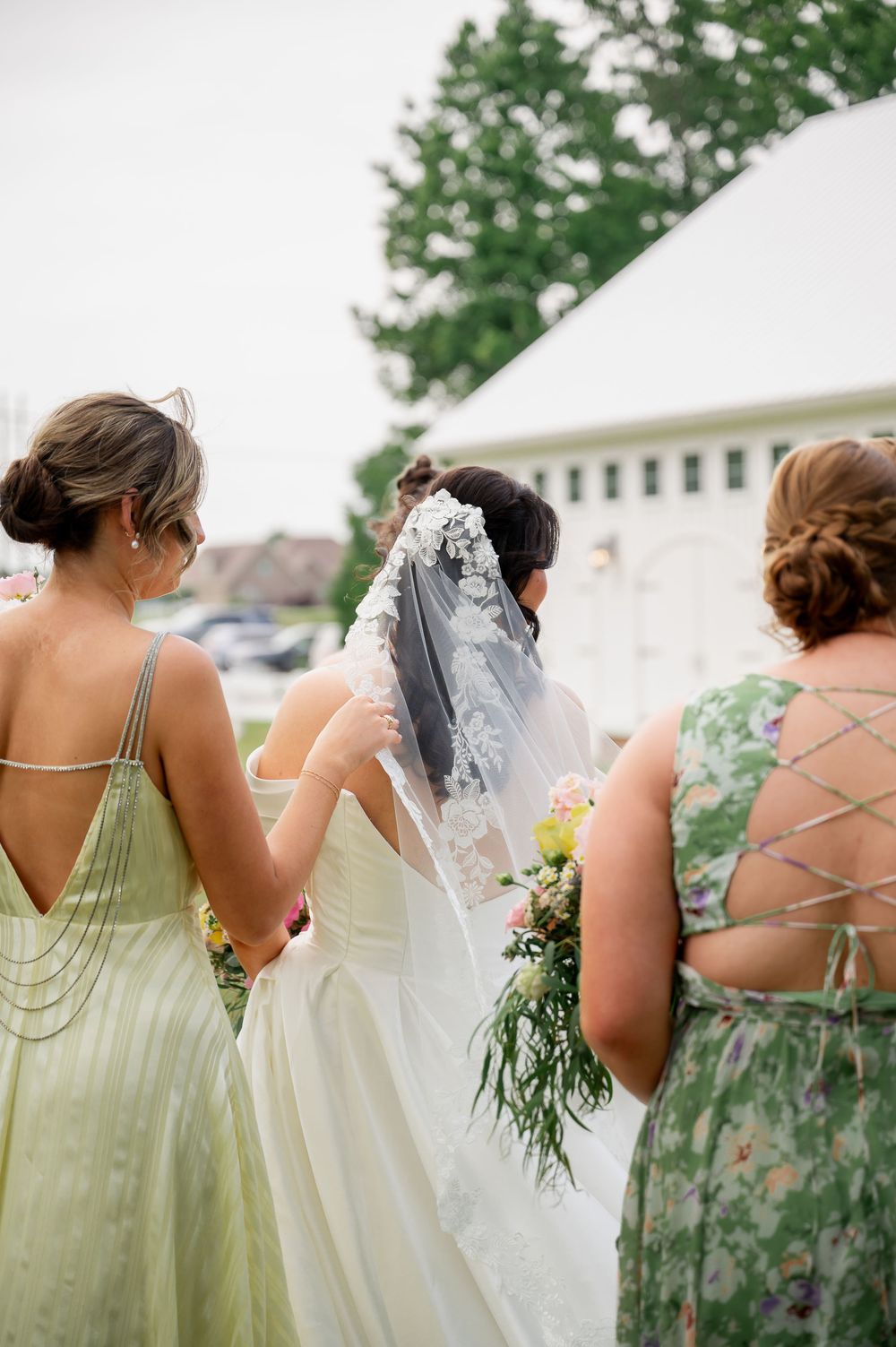 Back view of bridesmaids in pastel dresses standing in a row outdoors.