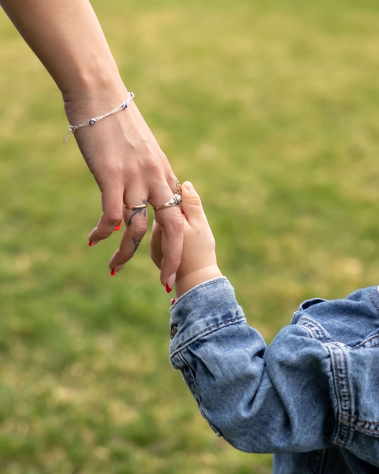 A hand wearing rings and red nail polish gently holds the cuff of a denim jean leg.