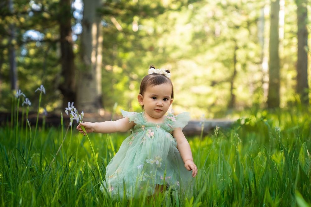 Child in mint green dress playing in a sunlit meadow with tall grass.