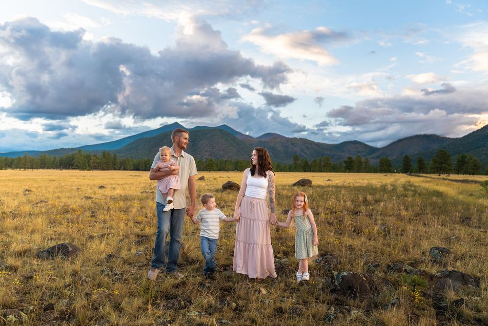 Family gathering in mountain meadow with dramatic cloudy sky and mountain peaks.