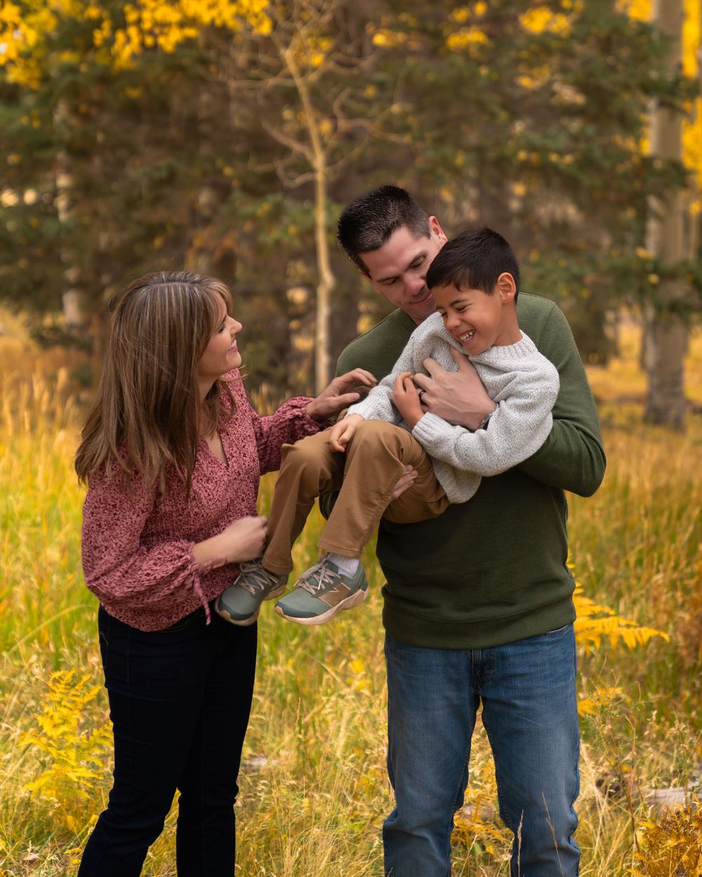 Family members share playful moments together in a golden-lit aspen forest during autumn.