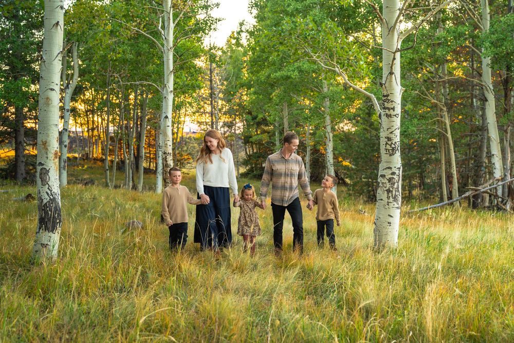 Family members gather for photos among white aspen trees in a grassy meadow at sunset.