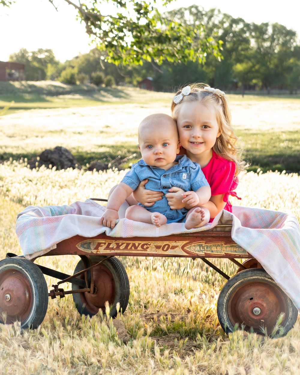Children laying together on a vintage red Radio Flyer wagon in a sunlit field.
