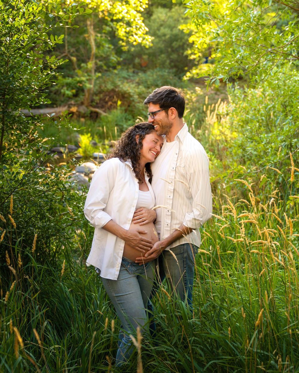 Romantic couple embracing in tall grass with sunlit trees in the background.