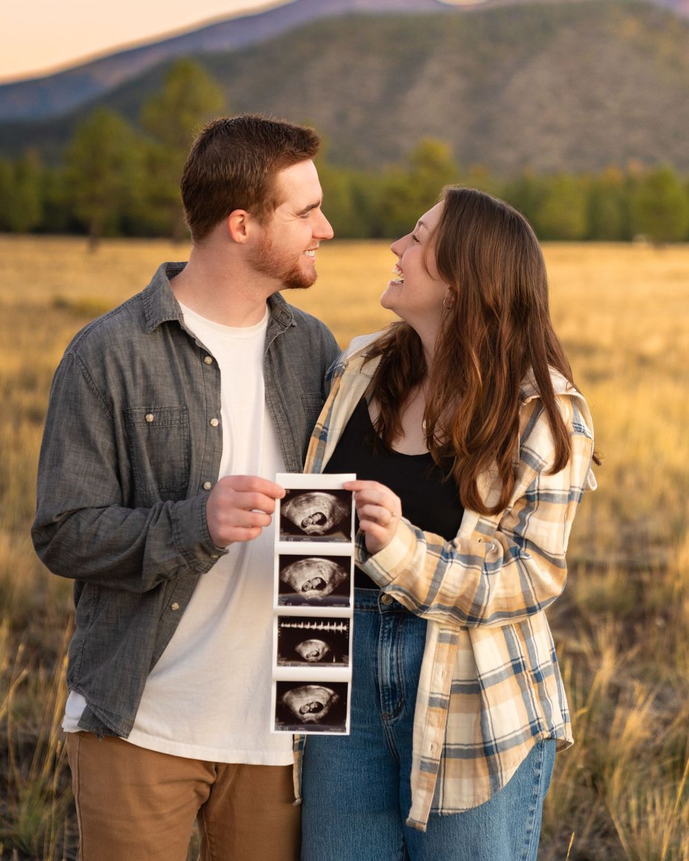 Couple sharing an intimate moment while holding ultrasound photos in a rustic outdoor setting.