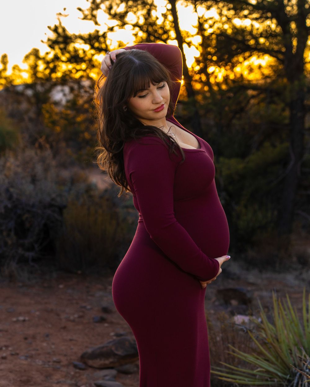 Maternity photoshoot in burgundy dress against desert landscape at golden hour.