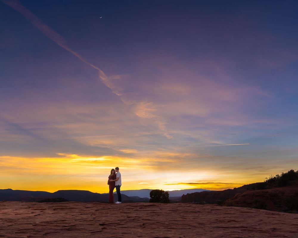 Desert landscape transitions from deep blue to golden sunset with red rock formations in distance.