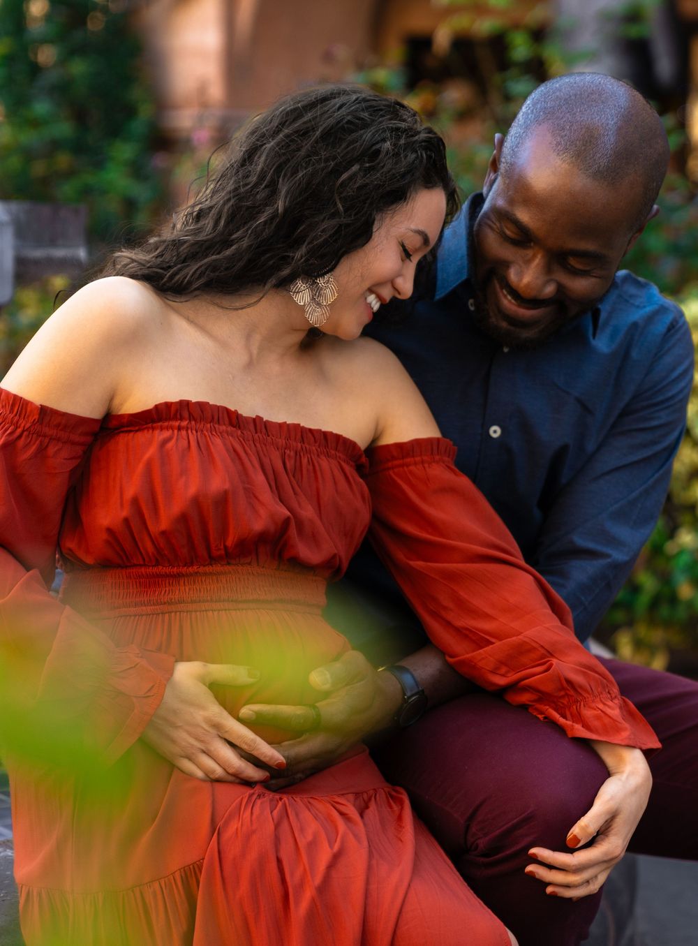 Couple in red dress and navy outfit share intimate moments in a garden setting.