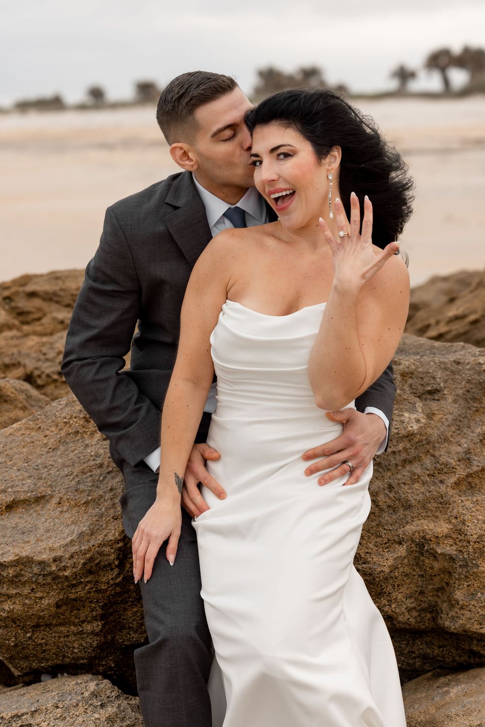 Romantic couple poses together on rocky beach during sunset wedding photoshoot.
