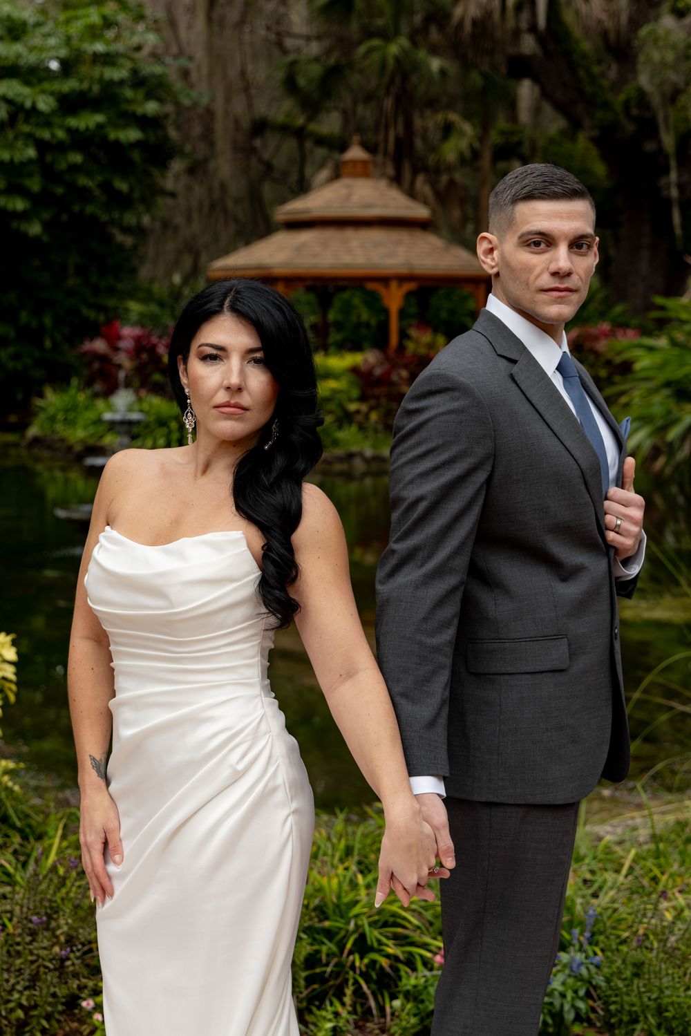Wedding couple poses in a lush garden setting with a gazebo in the background.
