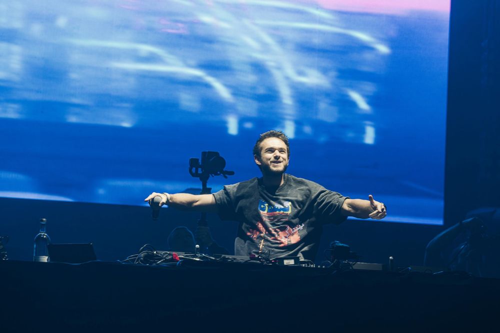 DJ performs on stage with dramatic blue lighting and fog effects at an electronic dance music festival.