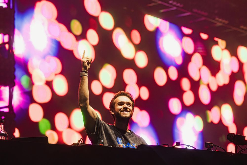DJ performs at a music festival with colorful bokeh lights creating a vibrant backdrop on stage.