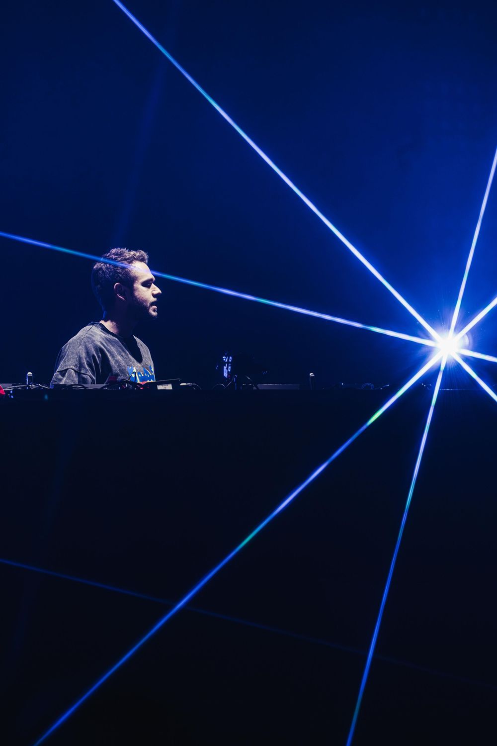 Blue laser beams cut through darkness creating geometric patterns at an electronic music performance.